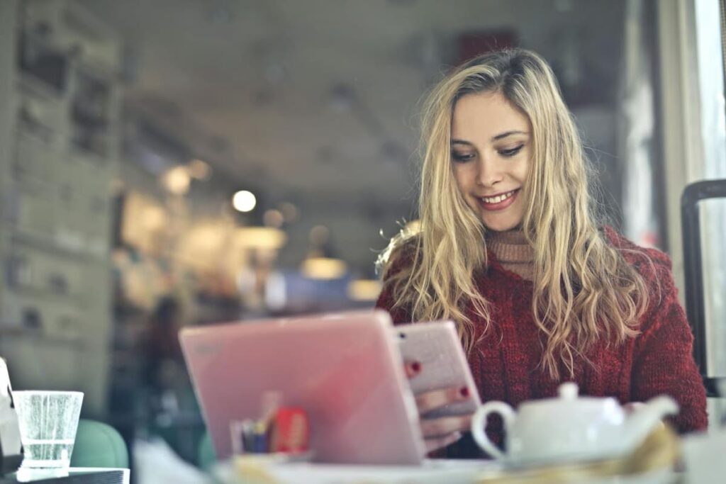 Imagem de uma mulher sorrindo olhando o celular em uma cafeteria
