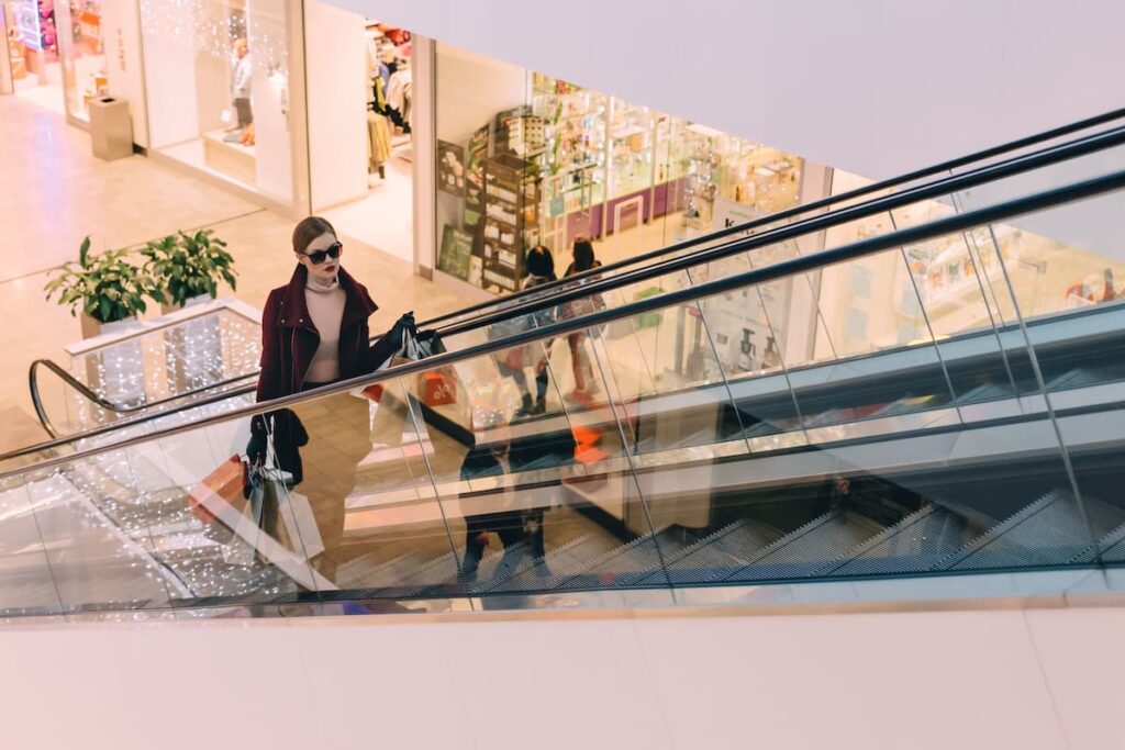 Mulher subindo uma escada no shopping com diversas sacolas