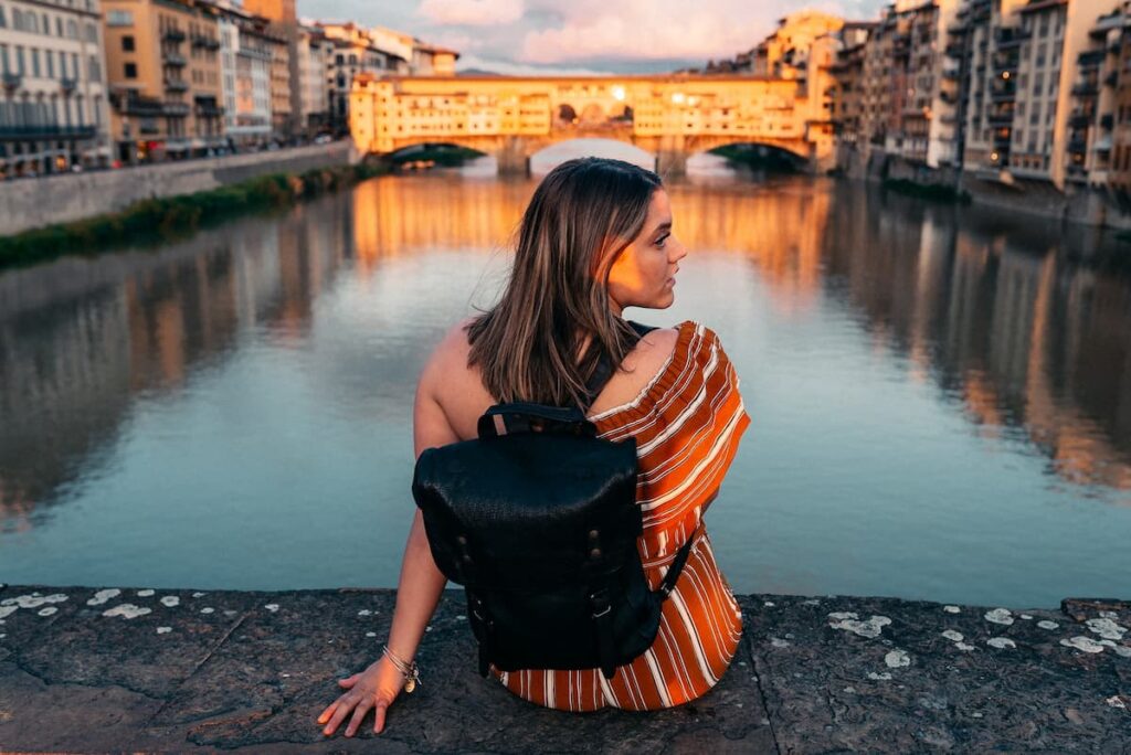 Imagem de uma mulher viajando de mochila sentada na frente de um canal
