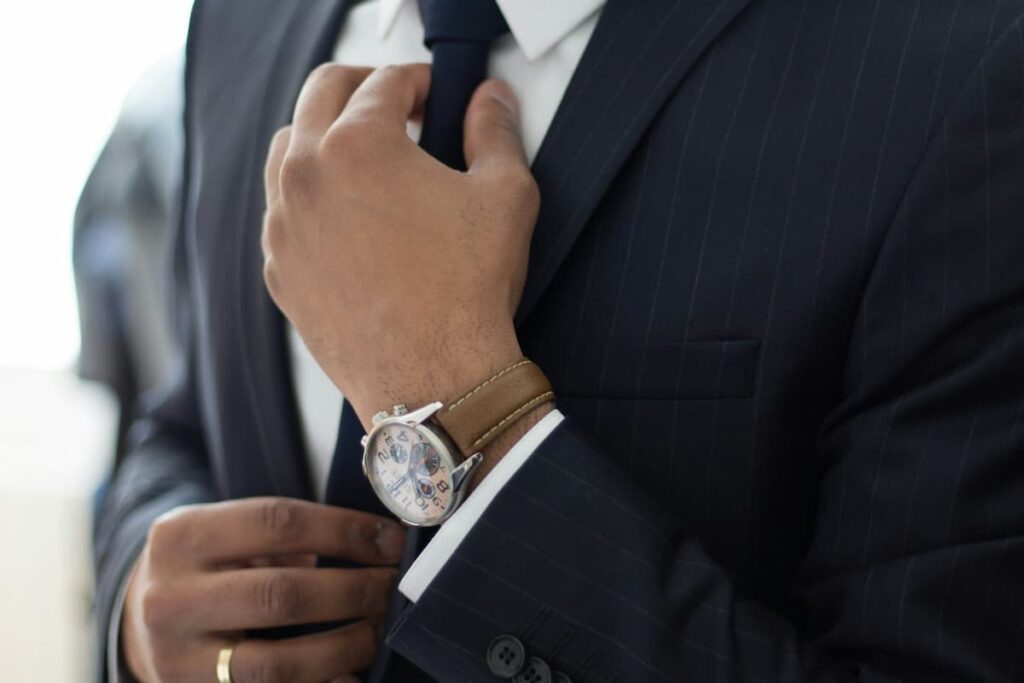 Imagem de um homem de terno mexendo na gravata com um grande relógio no pulso