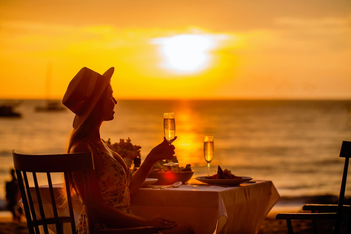 Imagem de um casal tomando champagne olhando o pôr do sol na praia