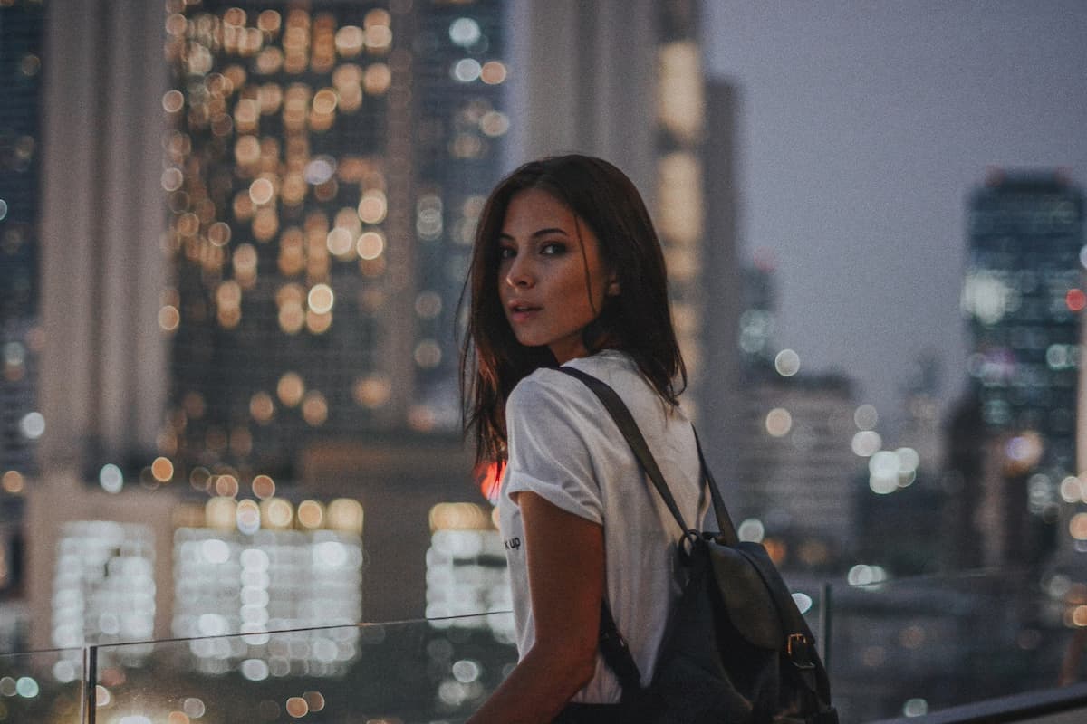 Imagem de uma mulher de mochila com prédios iluminados atrás