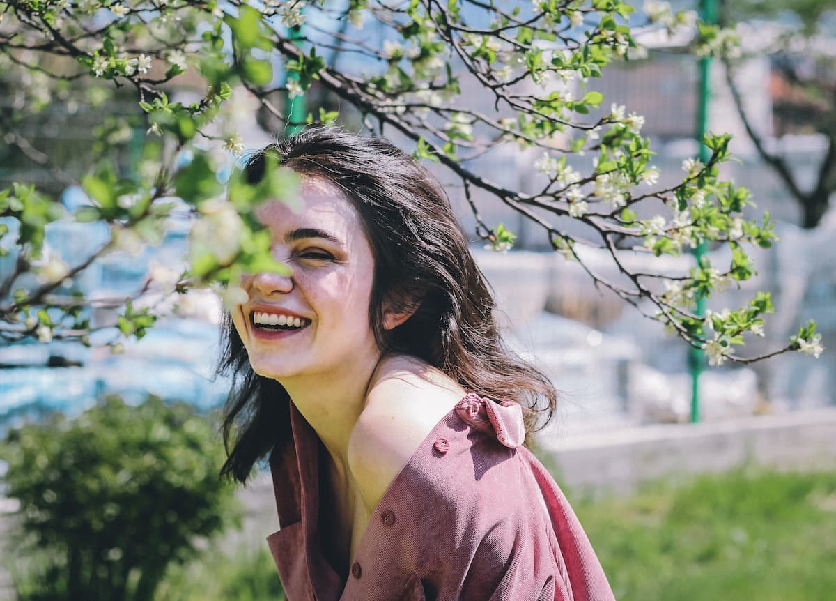 Imagem de uma mulher sorrindo do lado de uma árvore